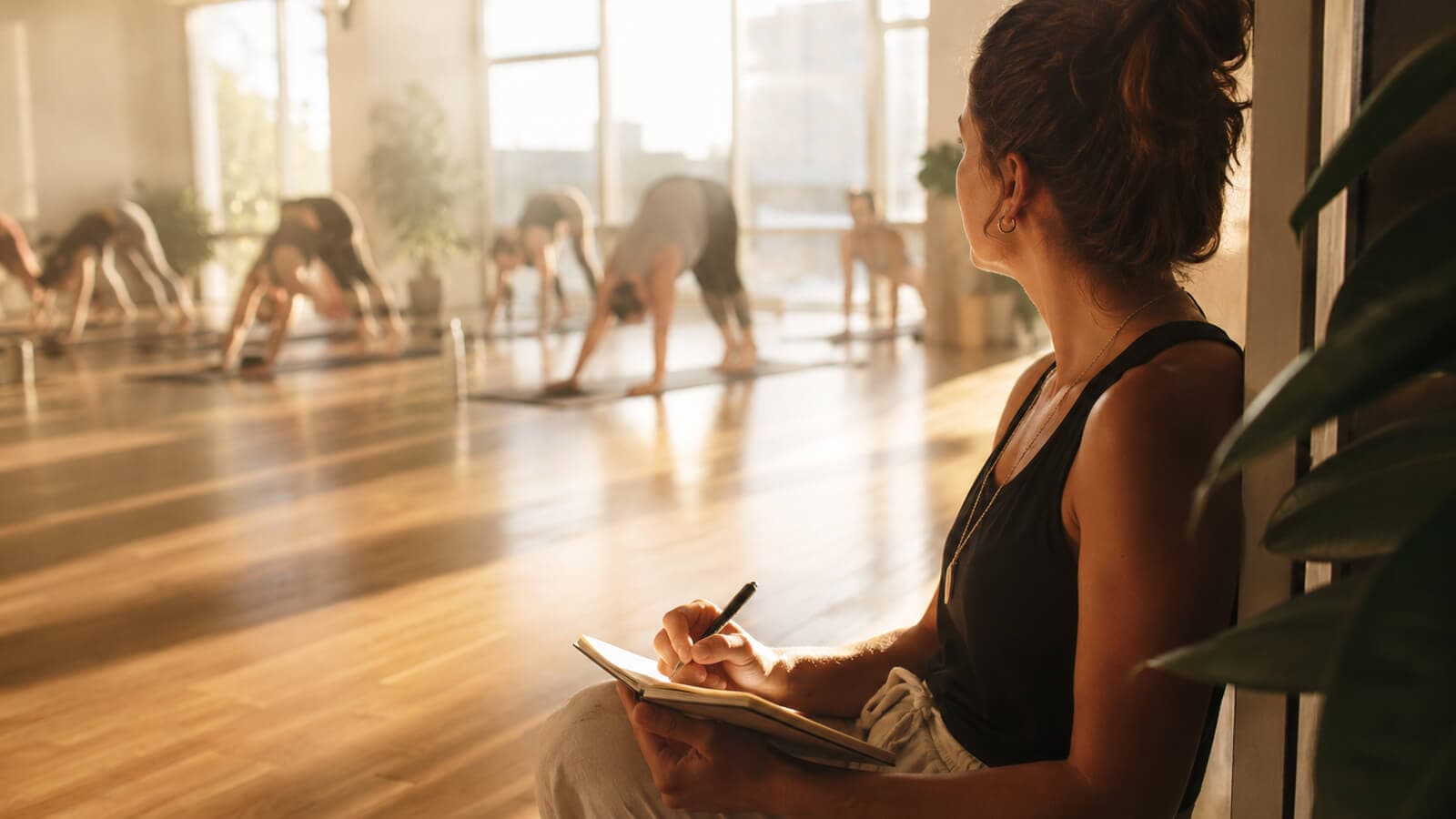 A reviewer taking notes at the side of a sunlit hot yoga class